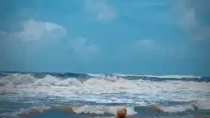 Tik Tok. Beach Voyeur looks on Blonde Teen enjoying Topless in the waves.